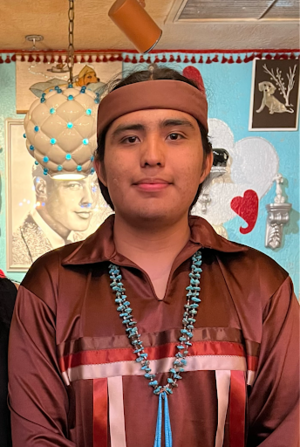 Falcon Reed (Tohono O'odham and Diné) pictured wearing a tan headband, wearing a maroon ribbon shirt with large turquoise beads, 