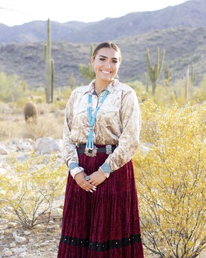 Lainey Tsosie (Diné) pictured in traditional regalia and adorned in turquoise in front of a desert