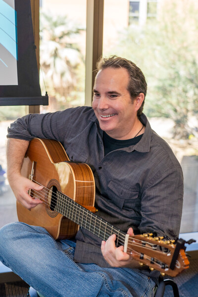 Musician Phillip Epey smiling while strumming guitar